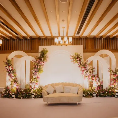 A clean and elegant stage for an engagement party, featuring white arched backdrops adorned with delicate pink and purple floral arrangements.