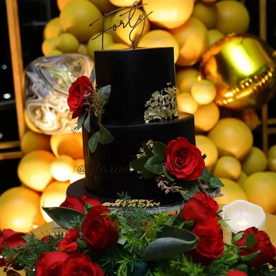 A stunning two-tiered black cake for a 40th birthday celebration. The cake is elegantly decorated with deep red roses and flecks of gold leaf, topped with a "Forty" sign, making it a sophisticated centerpiece.