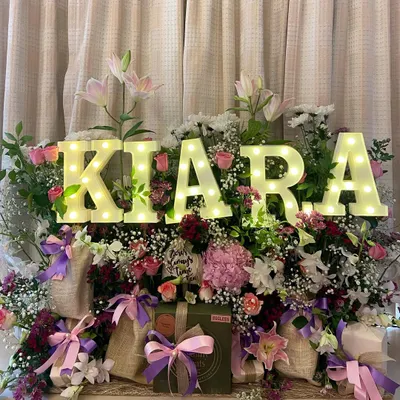 Celebrating a birthday should be as unique as the person themselves. This stunning floral hamper, personalized with the name 'Kiara' in glowing marquee letters, is designed to be an unforgettable centerpiece for any celebration.