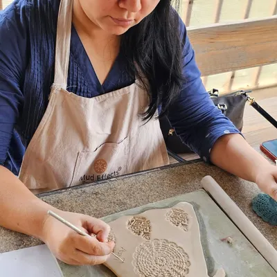 A student in a corporate workshop carefully carving intricate patterns into a clay slab. Hand-building allows for so much creativity and detail.