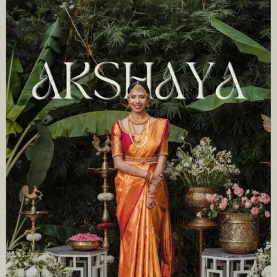A beautiful bride stands before our traditional South Indian photo booth, complete with brass lamps, banana plants, and classic floral arrangements.