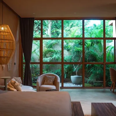 Unwind in the lap of luxury in one of my premium suites, featuring earthy tones and a large window with a garden view.