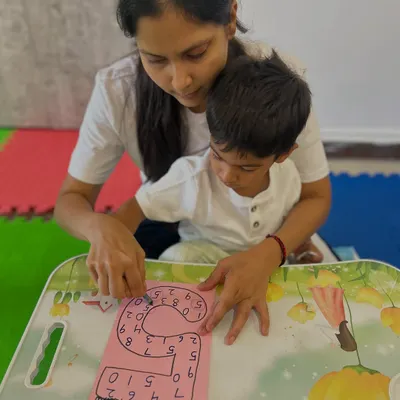 A mother and child work together on a number tracing worksheet. This guided activity helps with number recognition and pre-writing skills.
