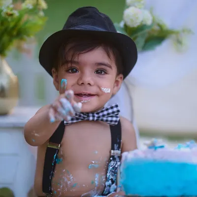 The best part of a cake smash is getting your hands messy. This close-up shot captures the pure joy and curiosity of a first birthday celebration, complete with a stylish bow tie and suspenders.