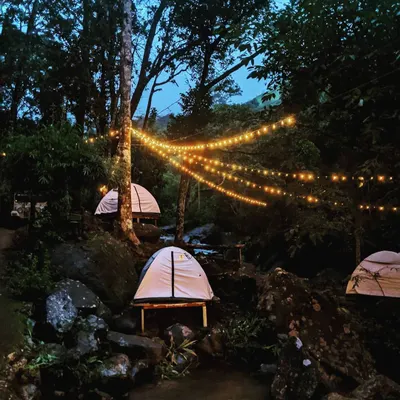 To add a touch of magic to the woods, I often string up warm fairy lights. Here, tents are nestled among the rocks and trees by a stream, creating an enchanting atmosphere as dusk settles in.