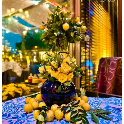 A classic Sicilian tablescape I designed, featuring a vibrant blue and white patterned tablecloth, a centerpiece of yellow roses and a lemon tree, and fresh lemons scattered for a rustic touch.