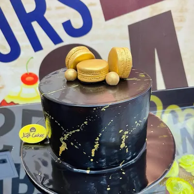 A chic and modern cake featuring a black marble fondant effect with artistic gold splatters. The design is finished with three elegant gold macarons on top, making it a perfect centerpiece for a sophisticated event.