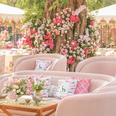 A stunning outdoor lounge setup with plush, curved pink sofas arranged around a tree adorned with cascading pink and white flowers. This creates a natural and breathtaking focal point.