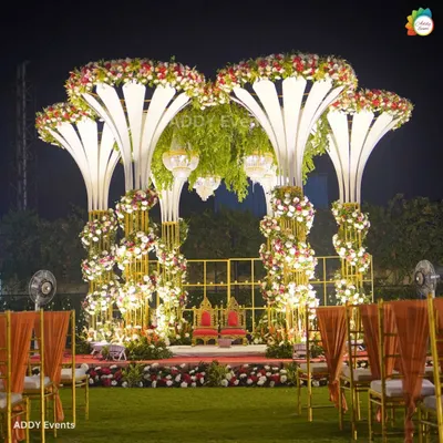 A mandap that commands attention. This magnificent structure features illuminated floral-inspired pillars, a canopy of lush greenery, and suspended crystal chandeliers, creating a royal setting for an unforgettable night wedding.