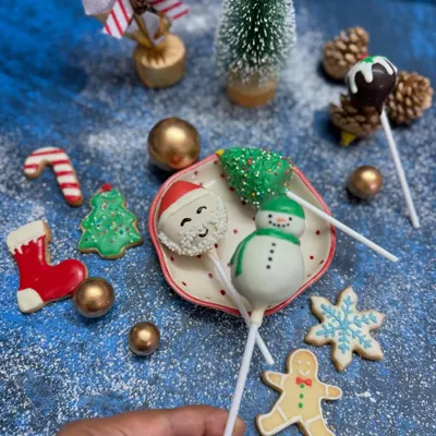 Our Christmas cake pops and cookies are perfect for spreading holiday cheer. This festive flat lay shows our hand-decorated Santa and snowman cake pops alongside an assortment of gingerbread and sugar cookies, ready to be part of your celebrations.