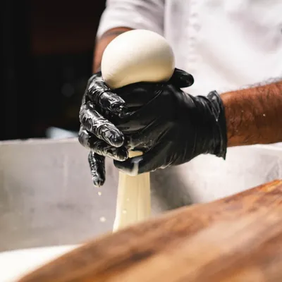 The final step in making our fresh mozzarella. A chef expertly squeezes the stretched curd to form a perfect, smooth ball of cheese.