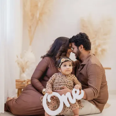 The big number one. This little girl, celebrating her first birthday, sits in front of her parents holding a "One" sign, creating the perfect announcement photo for this special milestone.