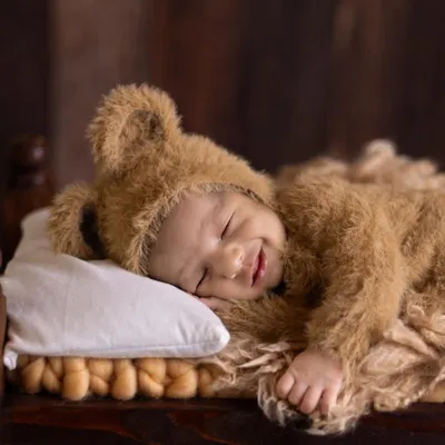 A heartwarming close-up of a smiling newborn dressed in a fuzzy teddy bear outfit, sleeping soundly on a tiny pillow. This shot captures the pure, innocent joy of a sleeping baby.