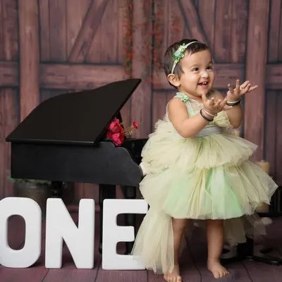 The pure happiness of turning one! This little princess in her beautiful green dress, clapping her hands with joy next to a mini piano, is what first birthday photoshoots are all about.