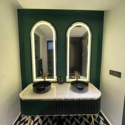 This completed bathroom balances classic and modern elements with its arched, backlit mirrors, a custom green fluted vanity, and striking geometric floor tiles.