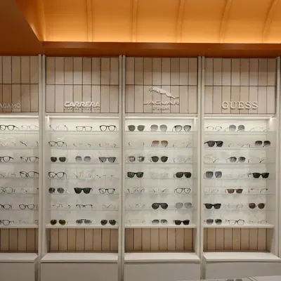 The full expanse of the eyewear display at 'The Brick Vault', showing the clean, illuminated shelving set against vertically laid beige tiles, all under the warm glow of the vaulted ceiling.