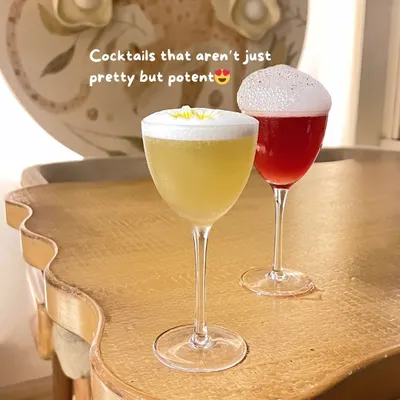 Two elegant cocktails on a uniquely shaped table, hinting at the stylish decor of the bar.