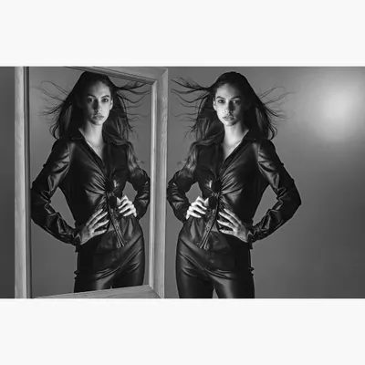 A conceptual black and white fashion portrait featuring a model in a leather outfit. The use of a mirror and wind creates a dynamic, high-energy image suitable for an edgy fashion editorial.
