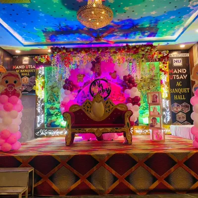 A grand stage setup for a naming ceremony in a banquet hall. The decor includes a royal-style sofa, Boss Baby character cutouts, and pink and white balloon pillars, creating a special spot for the main event.
