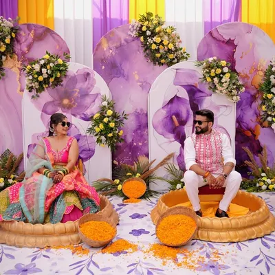 For this haldi, I designed a unique seating arrangement with the couple in separate ornate tubs, ready for the ceremony. The backdrop featured beautiful lavender and yellow watercolor panels with floral accents.