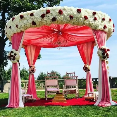 An elegant outdoor Vidhi Mandap we designed at a resort, featuring a beautiful floral canopy of white and red roses with flowing pink drapes. We create sacred and beautiful spaces for you to take your vows.