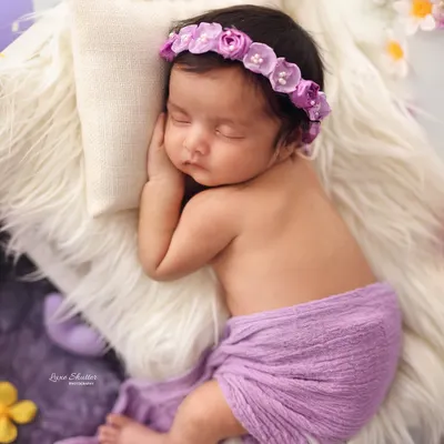 A close-up of a sleeping baby girl, adorned with a delicate purple floral headband to match her lavender-themed photoshoot.