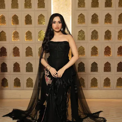A full-length editorial shot of actress Jannat Zubair for GlobalSpa Magazine. The image is set against an ornate, traditional backdrop, contrasting with her modern black couture gown to create a visually rich portrait.