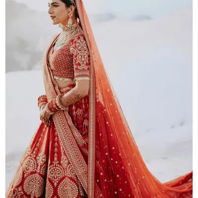 A powerful and elegant bridal portrait. The bride's striking red lehenga stands out against the stark white background, creating a high-fashion, editorial look.