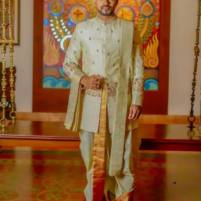 This is a complete look I designed for a South Indian groom. It features a layered, embroidered sherwani in a subtle off-white, paired with a traditional silk dhoti and shawl (angavastram) for a regal and authentic appearance.