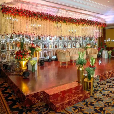 This reception stage is a floral fantasy. I created a massive backdrop wall with intricate white jaali niches holding candles, topped with a dense ceiling of hanging white and red flowers for a truly opulent and royal look at The Leela.