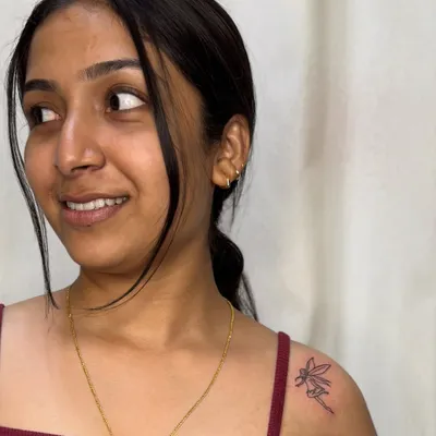 A delicate fine-line fairy tattoo on the shoulder. This minimalist piece captures a sense of magic and whimsy with just a few simple, elegant lines.