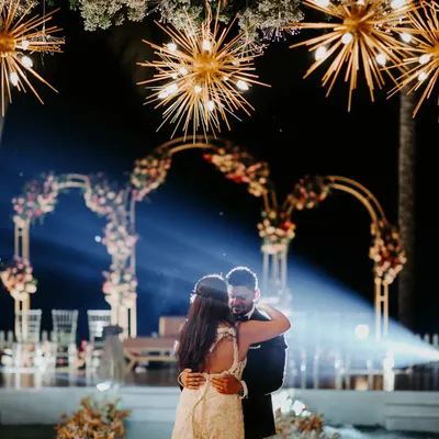 A magical first dance under a sky of starburst chandeliers. The combination of warm lighting, floral arches, and a touch of haze creates a truly cinematic and romantic reception moment.