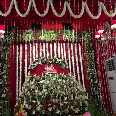 A full view of our Radha Ashtami decor, featuring a grand floral stage for the deity. We used a combination of red, white, and green flowers against a rich maroon fabric backdrop to create a traditional and opulent look.