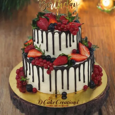 A delicious two-tier drip cake, generously topped with fresh strawberries, blueberries, and red currants. It's the perfect blend of elegance and freshness.