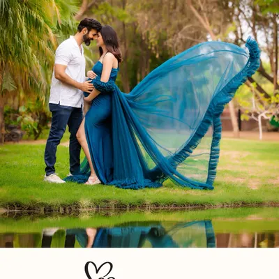 A breathtaking outdoor shot by the water, with the reflection adding a magical quality. The wind catches the mother-to-be's blue gown, creating a moment of pure drama and beauty.