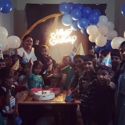 Even a simple setup can bring so much joy. Here, we created a fun party atmosphere with a blue and white balloon backdrop, a glowing neon 'Happy Birthday' sign, and party hats for all the kids to enjoy the cake-cutting ceremony.