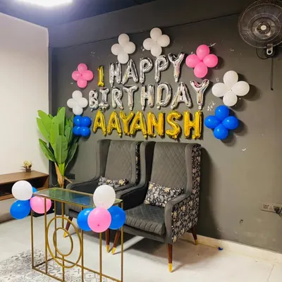A simple and elegant wall decoration for a first birthday at home. This setup uses foil balloons to spell out "Happy Birthday Aayansh" and is accented with small balloon clusters for a clean and modern look.