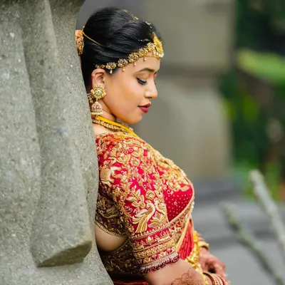 A moment of quiet reflection for the bride. Her custom red and gold saree, with its heavily embroidered blouse featuring peacock motifs, was designed to be a timeless piece of her wedding story.