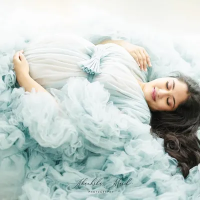 A moment of pure serenity. This overhead shot captures the mother-to-be enveloped in a cloud of soft blue tulle, creating a dreamy and peaceful fine art portrait.