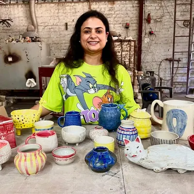 The wonderful result of a beginner's workshop. This student is proudly showing her first collection of handmade ceramic pieces, including mugs, bowls, and a very creative cat planter.