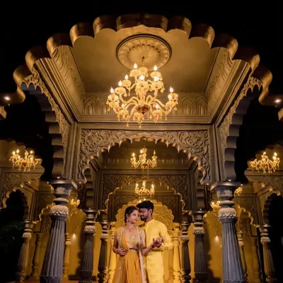 A couple stands in a majestic hall with golden lighting and intricate architecture. This shot is perfect for a royal-themed pre-wedding shoot.