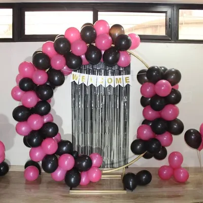 A fun and modern welcome home decoration. This setup features a circular frame with a pink and black balloon arch, a 'Welcome' banner, and a silver fringe curtain for a touch of sparkle.