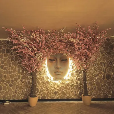 A dramatic installation featuring two large artificial pink cherry blossom trees framing a backlit sculpture. This creates a serene and artistic focal point in this hospitality space.