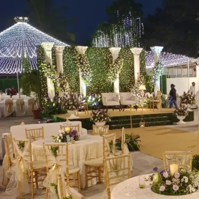 An evening reception at the Colaba Agiary. The space is illuminated by a canopy of fairy lights, with a grand stage featuring a green wall and classical pillars. The guest tables are elegantly set to complete the luxurious atmosphere.