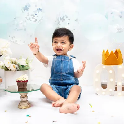 A first birthday cake smash is a momentous occasion. This little one, pointing up with a bit of cake on his face, is a perfect picture of curiosity and delight.
