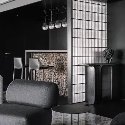 A full view of the bar in the Vaulted Haus, showing the Gabion wall facia, frosted glass brick partition, and custom pendant lights. The entire unit is conceived as part of a black 'scoop' that carves through the apartment's entrance.