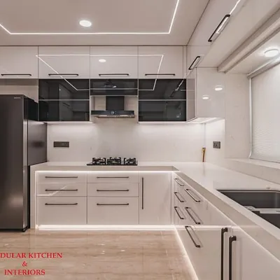 A stunning white modular kitchen in Mumbai Central, featuring an anti-scratch acrylic mirror finish and accents of grey-tinted glass. The high-gloss surface reflects light beautifully, making the space feel large and luxurious.