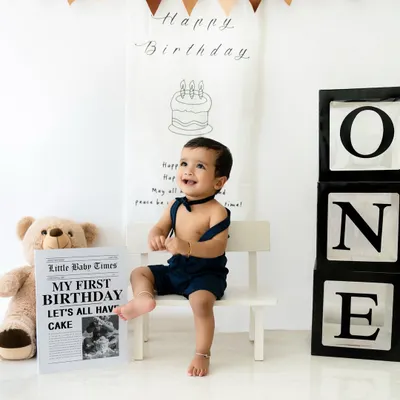 A perfect first birthday portrait. This little boy looks absolutely dapper in his bow tie and suspenders, sitting happily in a clean, modern setup with a teddy bear and "ONE" blocks.