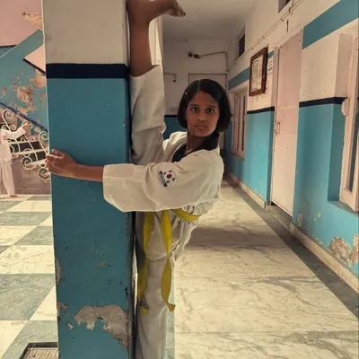 A young student with a yellow belt demonstrates an impressive standing wall split, showing amazing flexibility and control.