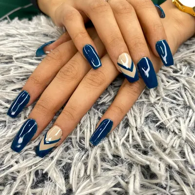 This manicure features a bold navy blue gel polish on long, coffin-shaped nails. The accent nails use a negative space technique with a nude base and sharp, geometric blue chevrons for a modern edge.